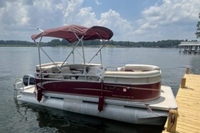 Pontoon boat docked on a lake under a partly cloudy sky.