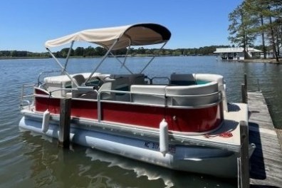 Red and white pontoon boat docked on a calm lake with clear sky.