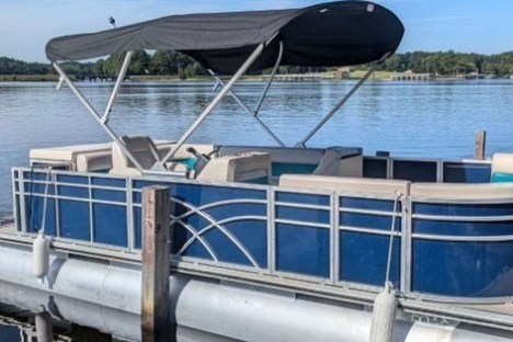 Pontoon boat with blue sides and black canopy docked on a calm lake.