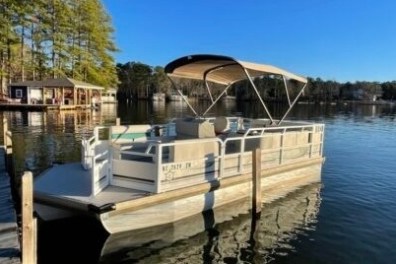 Pontoon boat docked on a calm lake under a clear blue sky.