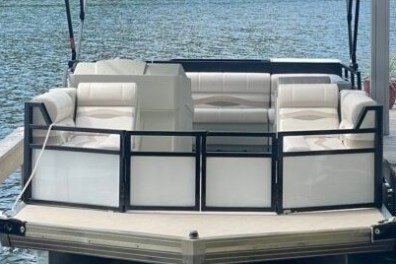 Pontoon boat docked, featuring beige seating and black railing on a calm lake.