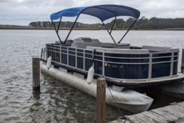 Pontoon boat docked on a lake with overcast sky.