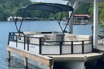 Pontoon boat docked beside a lakeside gazebo with trees in the background.