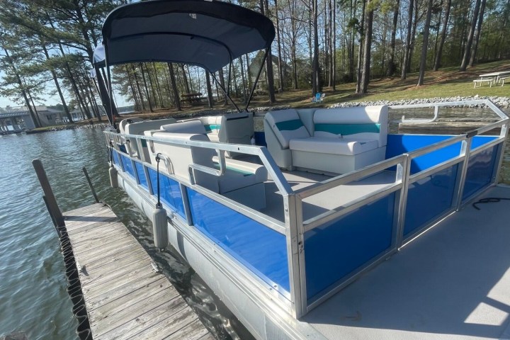 Pontoon boat with a blue canopy docked near a wooden pier on a lake.