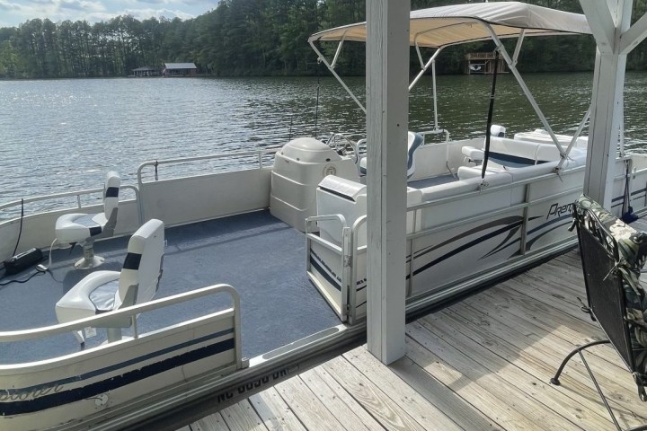 Pontoon boat docked at a lakeside wooden pier on a sunny day.