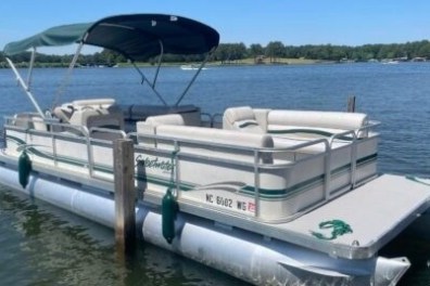 Pontoon boat with canopy on a lake, surrounded by trees and calm water.