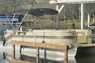 Pontoon boat docked by a lakeside gazebo on a sunny day.