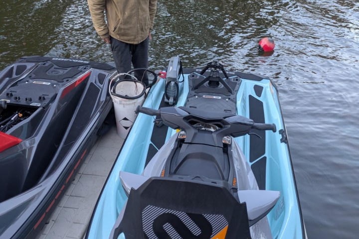 Person in a hoodie standing beside a docked jet ski by a lake.