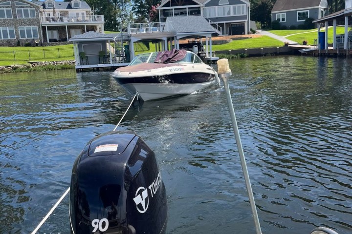 View of a motorboat towing another boat on a lake with houses in the background.