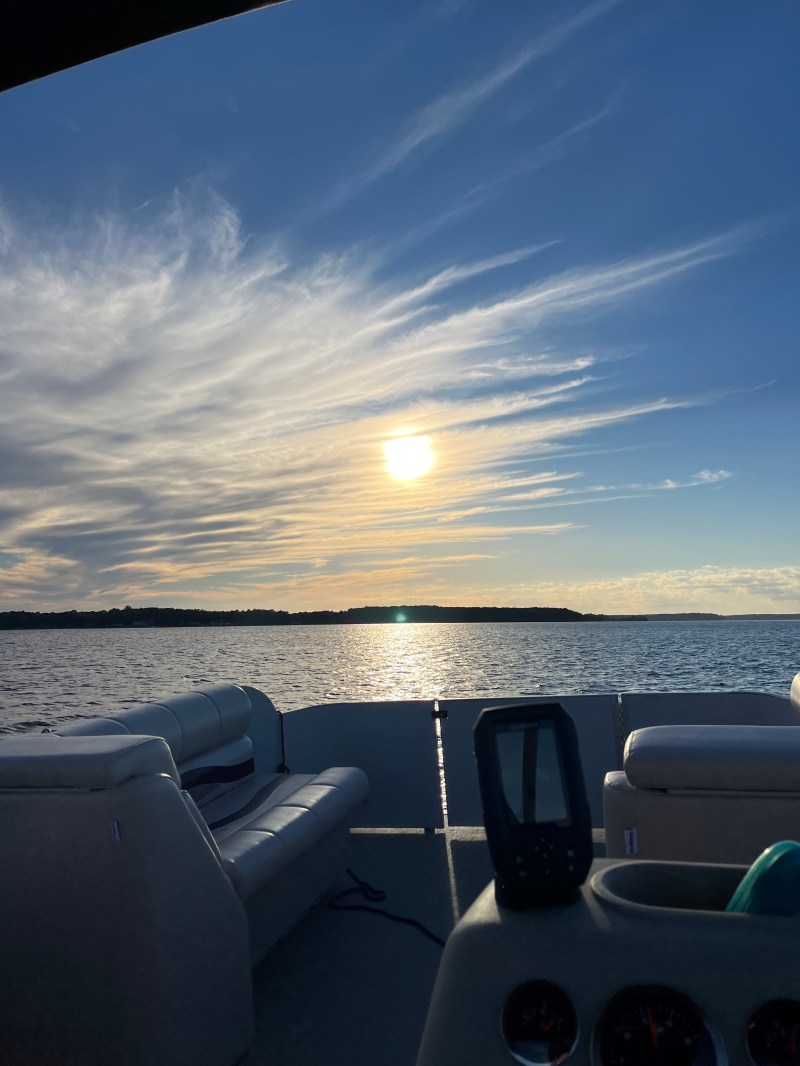 Boat interior facing a lake with a sunset, white clouds, and blue sky.
