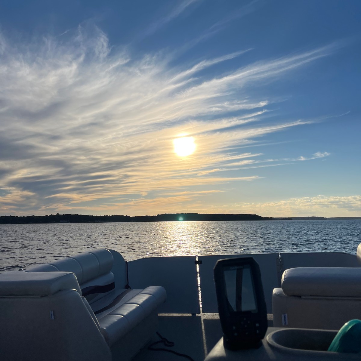 Boat interior facing a lake with a sunset, white clouds, and blue sky.