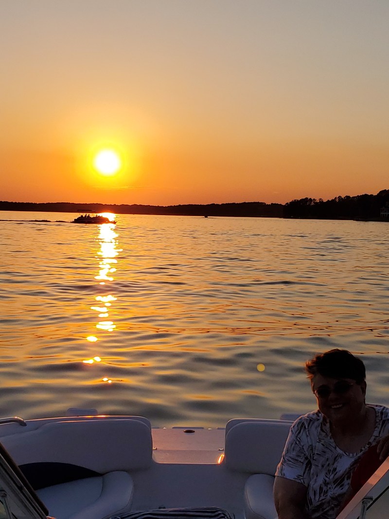 Three people on a boat at sunset, with calm water and a clear sky.