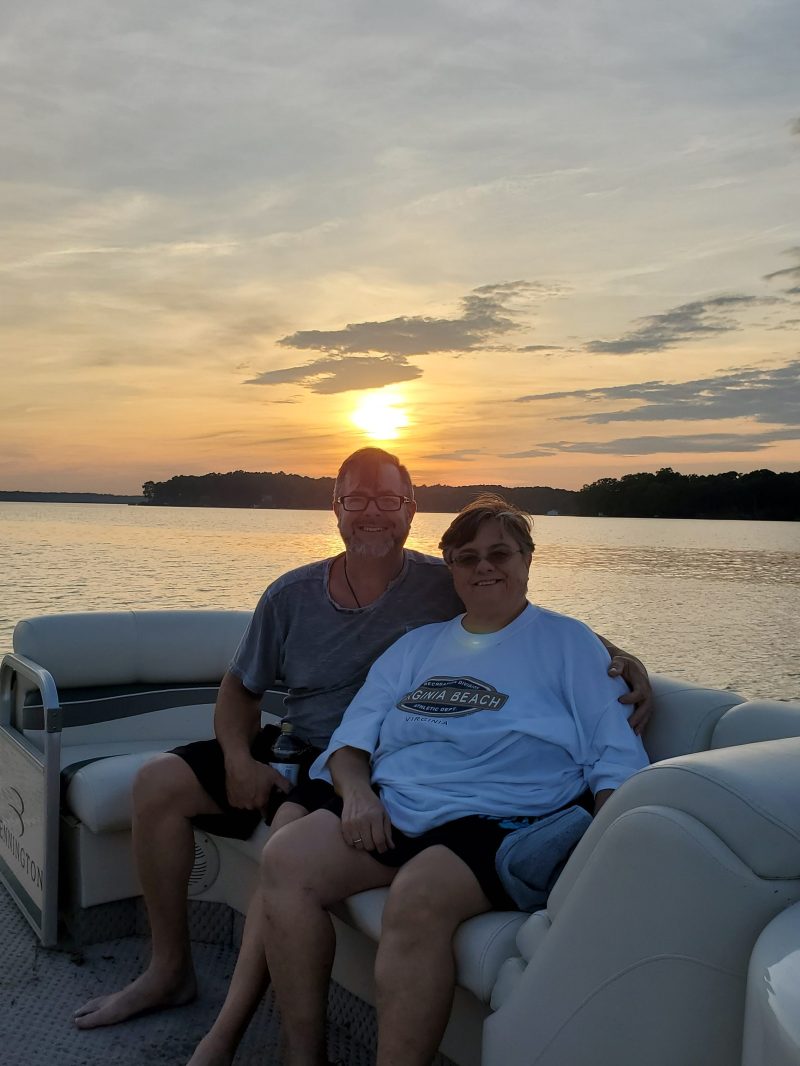 Two people sitting on a boat at sunset with a lake in the background.