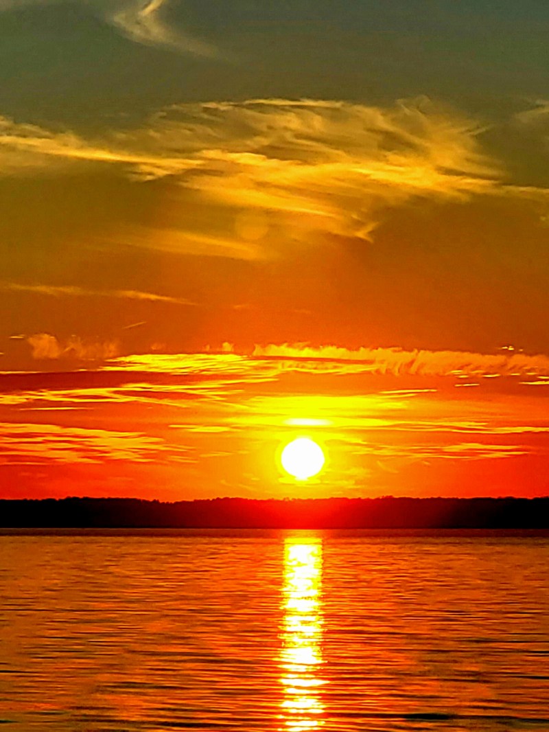 Vivid sunset over a calm lake with silhouetted trees and orange sky.